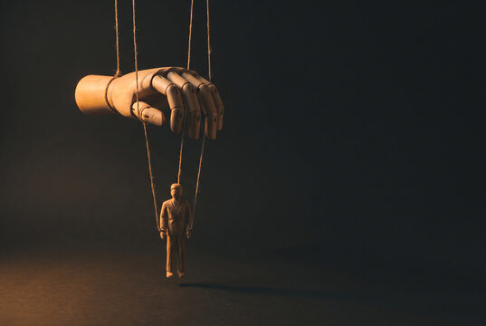 Marionette puppet under giant hand in a dark power control concept scene