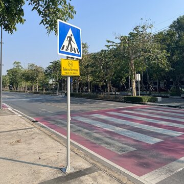 Pedestrian crossing with bicycle yield sign on a tree-lined urban road