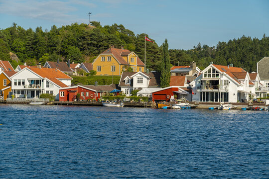 View of traditional white and yellow wooden houses with red roofs and small boats docked along the waterfront in Mandal, Agder, Norway.