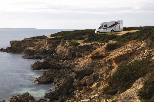 View of a white camper van parked on the rugged rocky cliffs of Capo Mannu overlooking the Mediterranean Sea in Sassari, Sardinia, Italy.