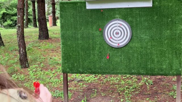 Woman throwing darts during an outdoor game in the forest. Casual recreational activity enjoyed among summer trees. Nature leisure scene showing precision and fun outdoors..