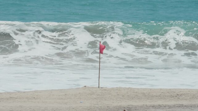 Red flag on a beach signaling danger as powerful ocean waves crash on the shore of puerto escondido
