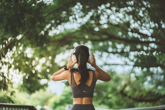 Sporty woman wearing headphones outdoors in green nature, fitness, music and active lifestyle concept