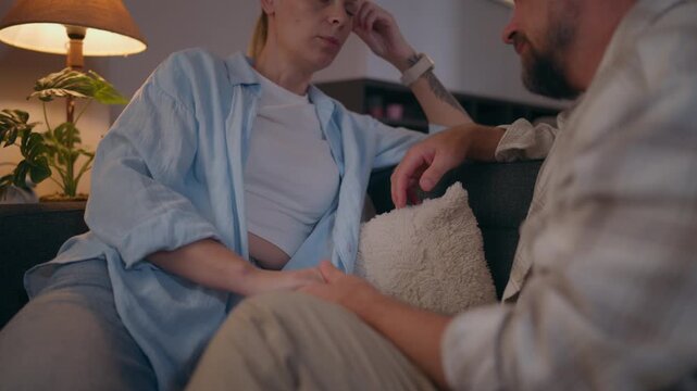 Couple having a serious conversation while sitting on a living room sofa, illustrating family tension, relationship conflict, emotional stress, disagreement and difficulties in communication.