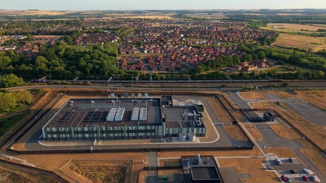 Aerial view of a hyperscale data center with rooftop cooling units near residential housing and railway tracks in Didcot, England, United Kingdom.