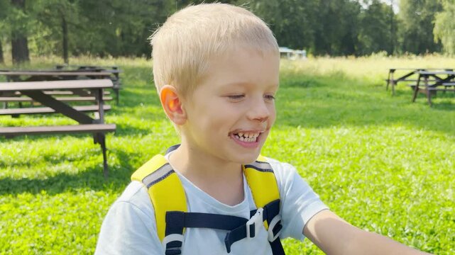 A young blond boy bites into an ice cream cone in a sunny green park. He feels happy, joyful, and excited during this sweet outdoor snack break.