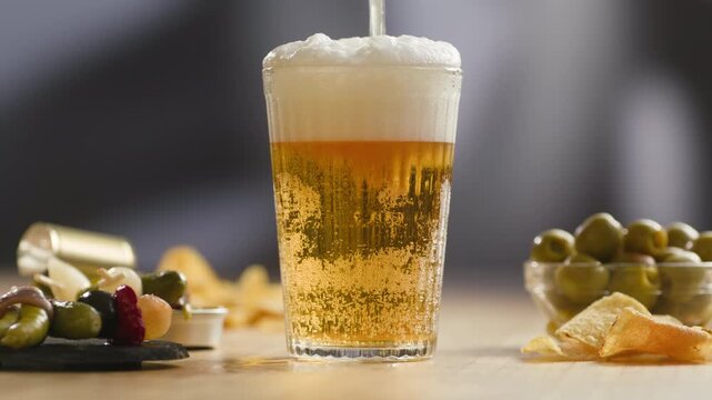 Fresh Spanish small beer served in a small glass with creamy foam at a traditional bar. Classic draft lager, authentic pub atmosphere, close-up food and drink
