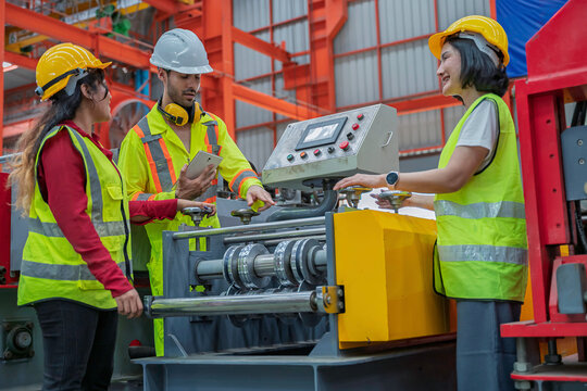 Industrial engineers set up and operate a metal forming machine in a factory. Concept of manufacturing, machine setup, engineering, teamwork, production, and industrial technology.