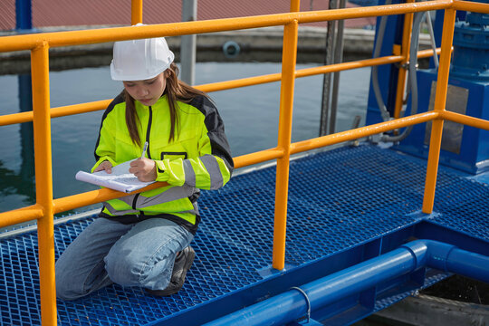Female engineer recording inspection data at a water treatment plant. Concept of water quality, utility operations, environmental engineering, infrastructure and safety.