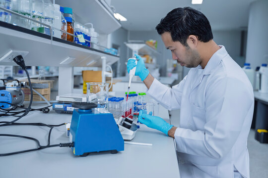 Male researcher looks at the camera while working in a modern scientific laboratory. Concept of research, laboratory science, biotechnology, experiments, analysis, and professional scientist.