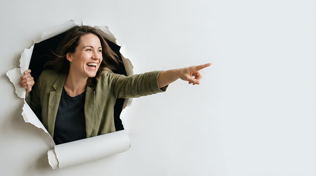 A woman wearing a green blazer enthusiastically tears through a white paper wall and points to an unseen destination.