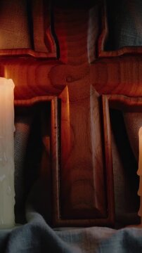 Vertical video: Flickering left candle flame lighting carved cross on altar, showing wax for prayer