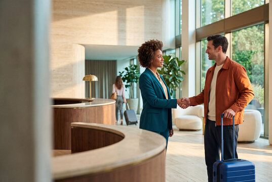 Boutique hotel manager welcoming a newly arrived guest with a handshake, representing hospitality, customer service and premium travel experience.
