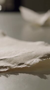 Vertical video: Shifting focus, torn paper sheet lifting edge, revealing fibers on reflective table