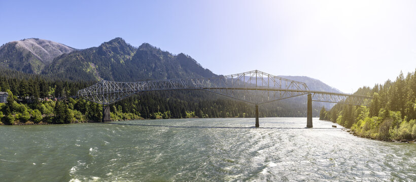 View of the Bridge of the Gods spanning the Columbia River with lush forested mountains in the background in Cascade Locks, Oregon, United States.