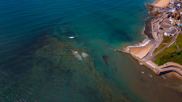 Aerial view of The Cobb and historic harbour in Lyme Regis, with the stone breakwater extending into the turquoise English Channel along the Jurassic Coast, Lyme Regis, England, United Kingdom.