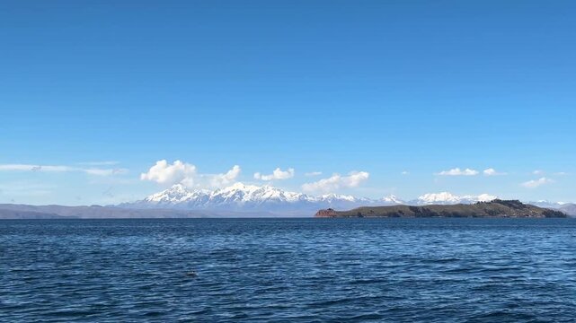 Vista panor&acirc;mica do Lago Titicaca com a Cordilheira Real e picos nevados ao fundo, Bol&iacute;via. Paisagem calma de &aacute;gua e montanhas dos Andes sob c&eacute;u azul.