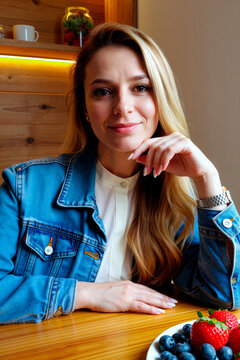 Portrait of Caucasian young adult woman sitting at cafe table, smiling at camera, suggesting approachable lifestyle branding. Ideal for hospitality marketing, personal brand content, vertical