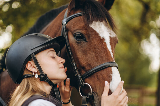 A young female equestrian stands near her horse and prepares for a competition.