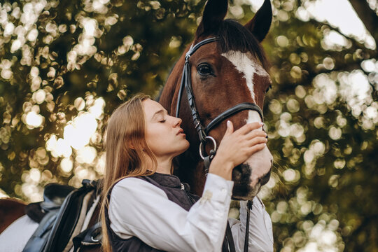 A young female equestrian stands near her horse and prepares for a competition.