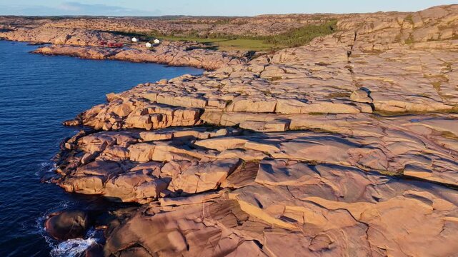 Aerial view of Ramsvikslandet Fykan rocky coastline with granite cliffs and calm sea during golden hour in Hunnebostrand, Vastra Gotaland County, Sweden.