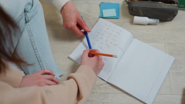 Student practicing grammar exercises in notebook, pencil and tutor hand pointing at sentences, cozy living room floor, soft natural light, casual clothes, focused guidance and corrective feedback