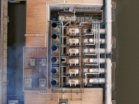 Aerial view of an industrial power plant with large tanks, complex piping, and exhaust stacks emitting smoke along a waterfront in Santo Domingo, Distrito Nacional, Dominican Republic.