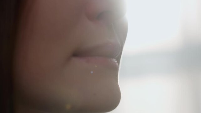 Closeup lips of white woman practicing pronunciation at home, soft backlight, subtle mouth movements and breath control for grammar coaching, focused diction rehearsal in calm intimate setting