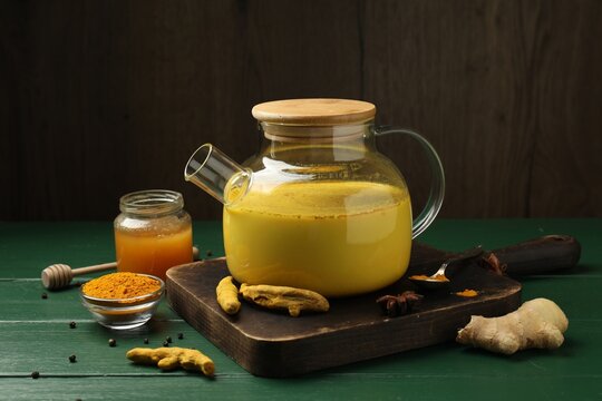 Golden milk turmeric latte in teapot and ingredients on green wooden table