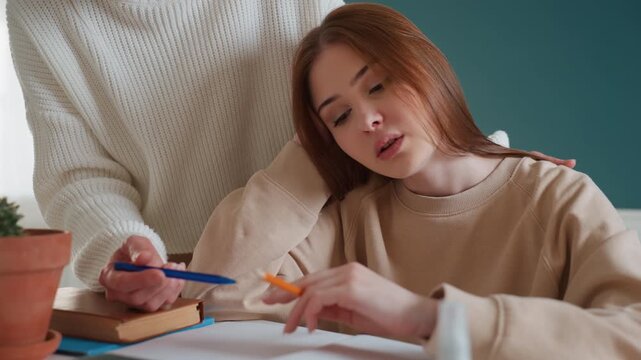 Caucasian tutor points at workbook with pen, closeup of home study session with notebook and pencil, female teen leaning on shoulder while tutor explains grammar and correction, soft lamp light,