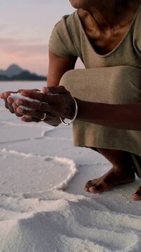 Vertical video: Walking senior woman to camera bending and scooping salt plain barefoot, copy space