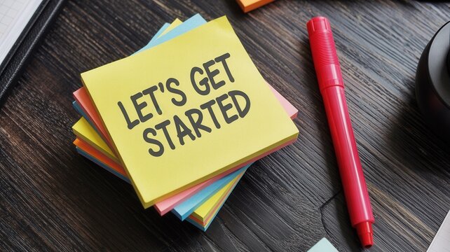 Let's Get Started text on sticky note pad with red marker on wooden desk top view