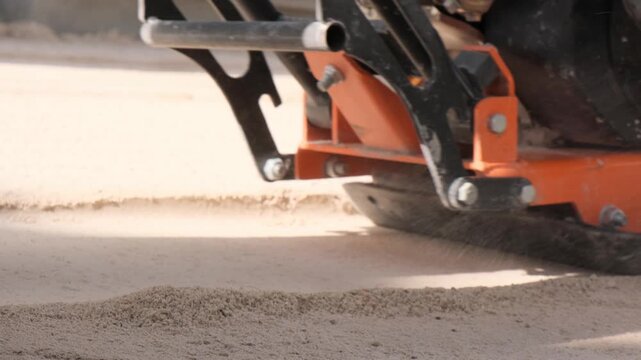 Low angle moving shot alongside a vibratory plate compactor preparing the base at a construction site, modern construction equipment and technology for building projects