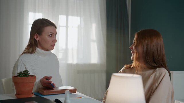 Home tutoring session caucasian tutor student discussing grammar homework at cozy desk, lamp glow, notebook and pen, plant on table, attentive tutor explaining rules while teenage student listens