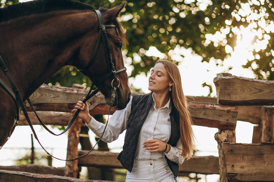 A young female equestrian stands near her horse and prepares for a competition.