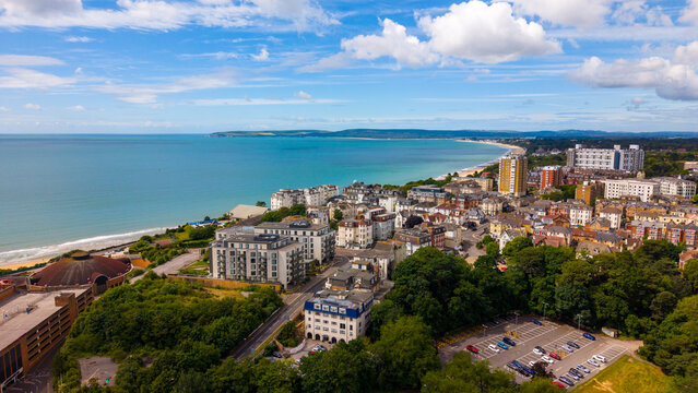 Aerial view of the Bournemouth coastline featuring the sandy beach, urban architecture, and lush greenery under a bright blue sky, Bournemouth, England, United Kingdom.