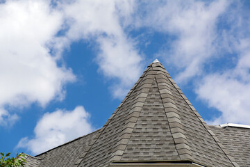 Gray asphalt roofing shingles on a pointed turret peak against a blue sky © Baharlou