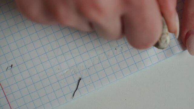 Closeup white womans hand erasing sentence marks on grid paper during focused grammar lesson, delicate kneaded eraser smoothing lines with precise thoughtful movements