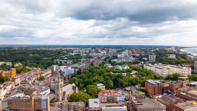 Aerial view of the urban landscape of Bournemouth featuring the historic church, dense greenery, and the distant coastline under a cloudy sky in Bournemouth, England, United Kingdom.
