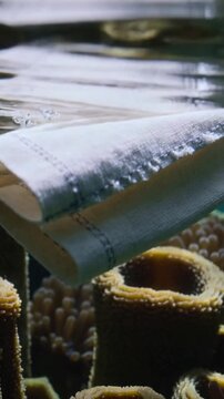 Vertical video: Folded panel stitched hem flexing from tank ripples, releasing bubbles over tubes