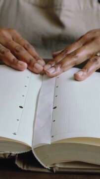 Vertical video: Hovering hands smoothing book gutter strip at table, flattening pages, beige top