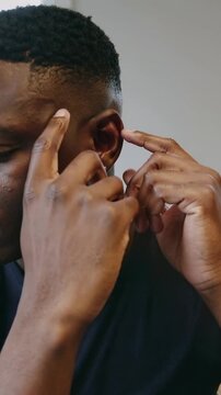 Vertical video: Bringing hands to ear, man guiding earbud into left ear in calm room, checking fit
