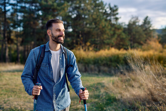 Hiking man enjoys nature with trekking poles in a lush forest during a sunny day