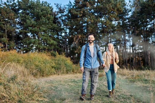 Hiking couple, young man and woman enjoys nature with trekking poles in a lush forest during a sunny day