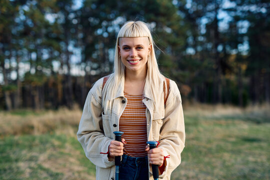 Hiking woman enjoys nature with trekking poles in a lush forest during a sunny day