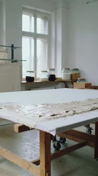 Vertical video: Unrolling canvas woman applying primer on studio table rolled sleeves, copy space