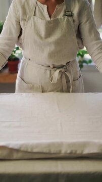 Vertical video: Placing folded linen, woman smoothing, tucking on kitchen counter for baking, apron