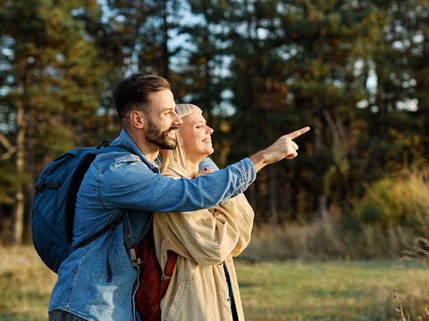 Hiking couple, young man and woman enjoys nature with trekking poles in a lush forest during a sunny day