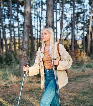 Hiking woman enjoys nature with trekking poles in a lush forest during a sunny day