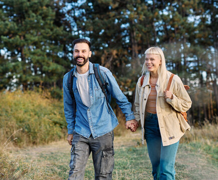 Hiking couple, young man and woman enjoys nature with trekking poles in a lush forest during a sunny day